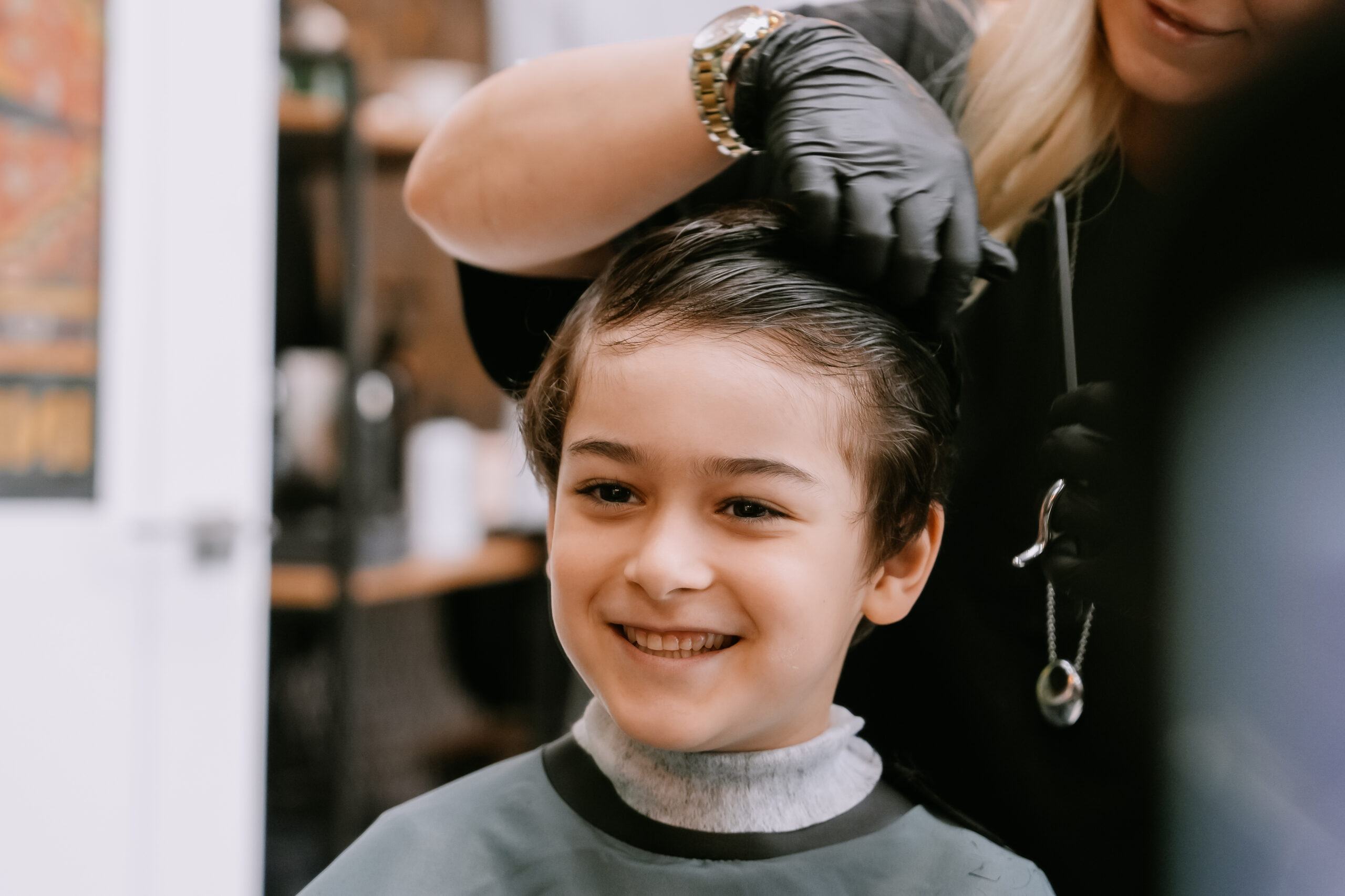 A cheerful boy smiles during a haircut, enjoying the experience with a friendly hairstylist attending to him.